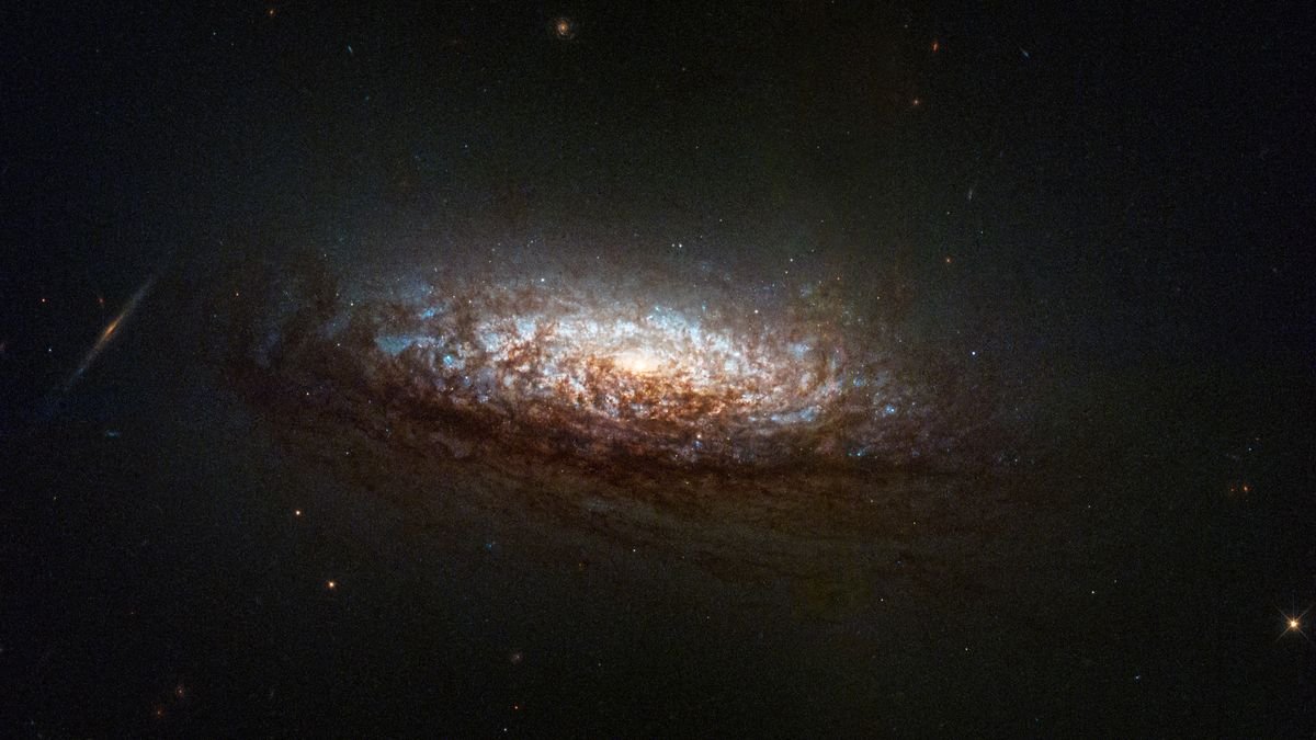 a stunning spiral galaxy hangs dimly in the dark of space a bright light at its center illuminates nearby gasses swirling around in shades of pale blues whites and crisp browns