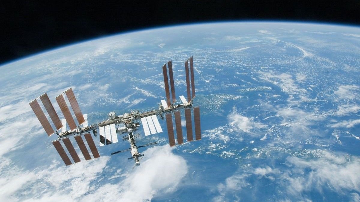 a T shaped space station with multiple solar arrays floats above earth