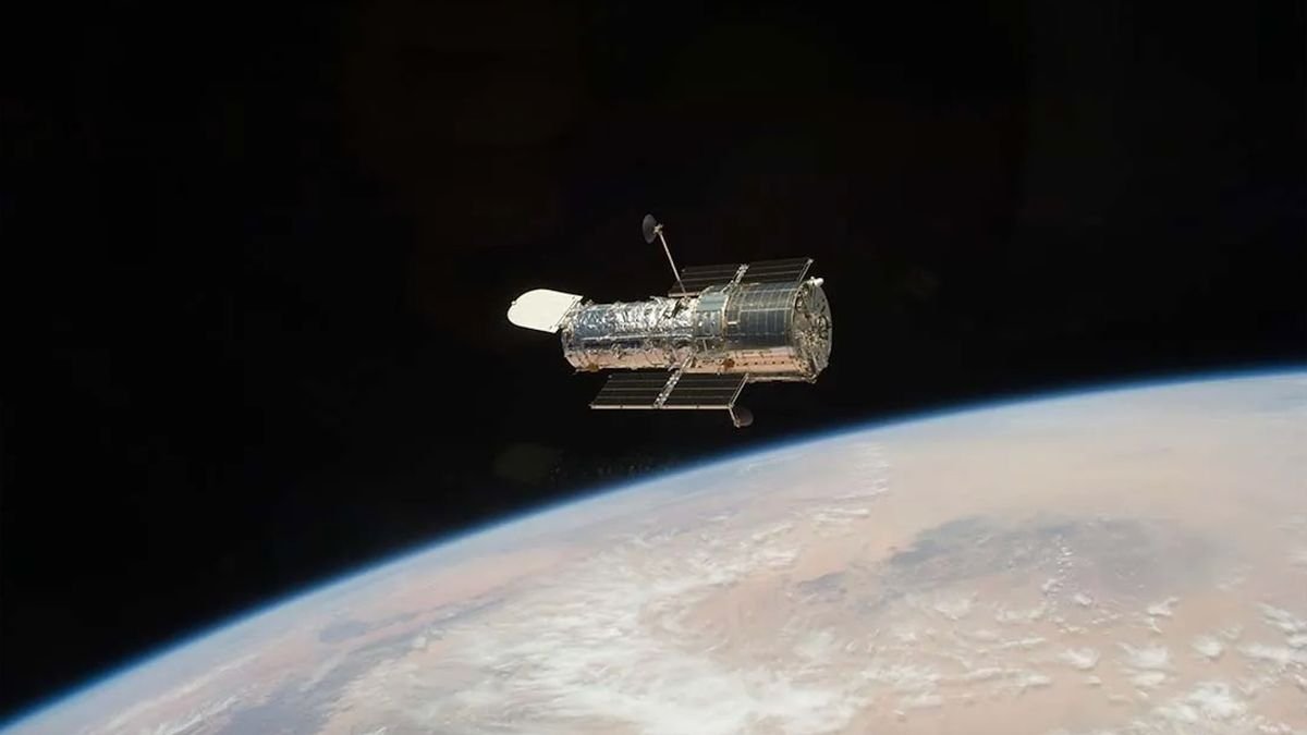 A metallic wrapped spacecraft in space which looks black above Earth