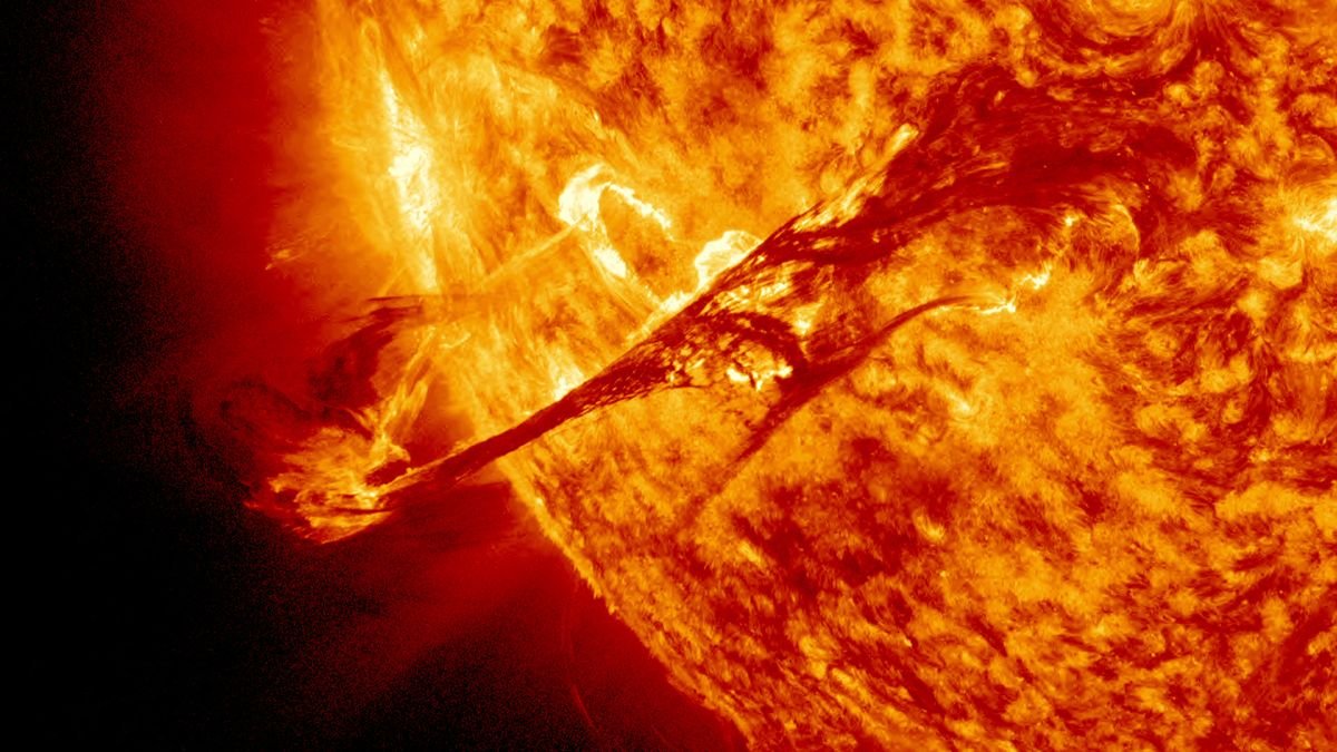 a raging fiery yellow and organge sun blazes from the right filling two thirds of the image the star spits an arch of plasma high above its surface so hot