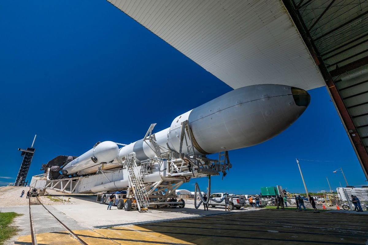 a large white rocket is transported horizontally toward its launch pad with a blue sky in the background