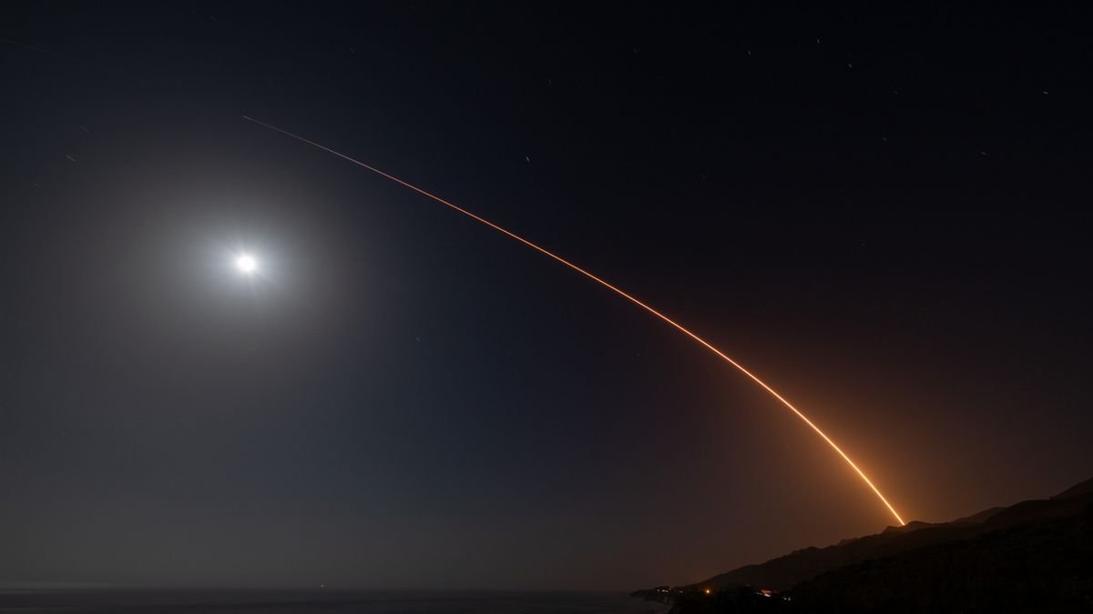 A rocket launch carves an orange arc into a dark night sky in this long exposure photo