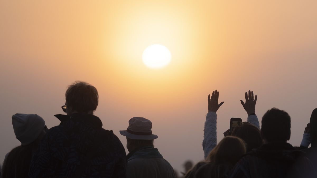 view of the sun shining through hazy cloud with people in the foreground looking towards the sun one person has both of their hands raised to the sky