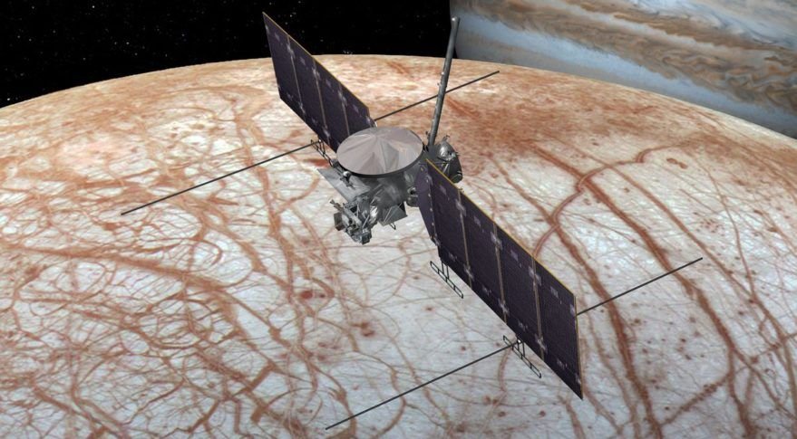 A spacecraft seen over a red streaked world Jupiter a striped and swirly looking world is in the background offscreen