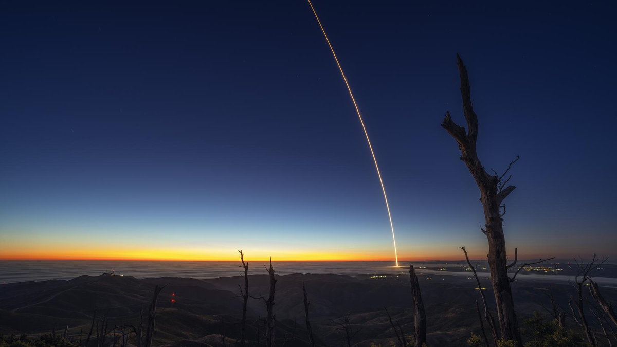 a rocket launches at night leaving a streak of light through the sky