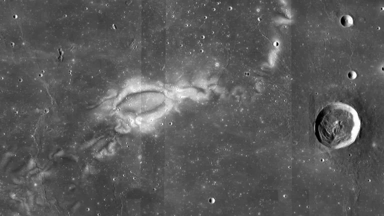 A dark grey high altitude view of the lunar surface with tiny craters speckled throughout and one large crater on the far right