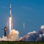 a black-and-white spacex falcon 9 rocket launches into a blue sky.