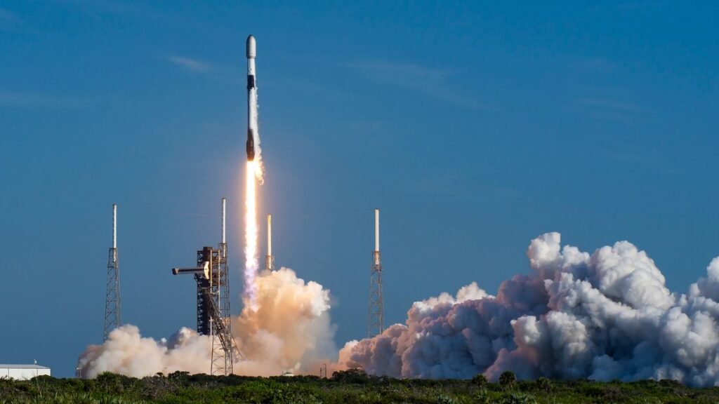 a black-and-white spacex falcon 9 rocket launches into a blue sky.