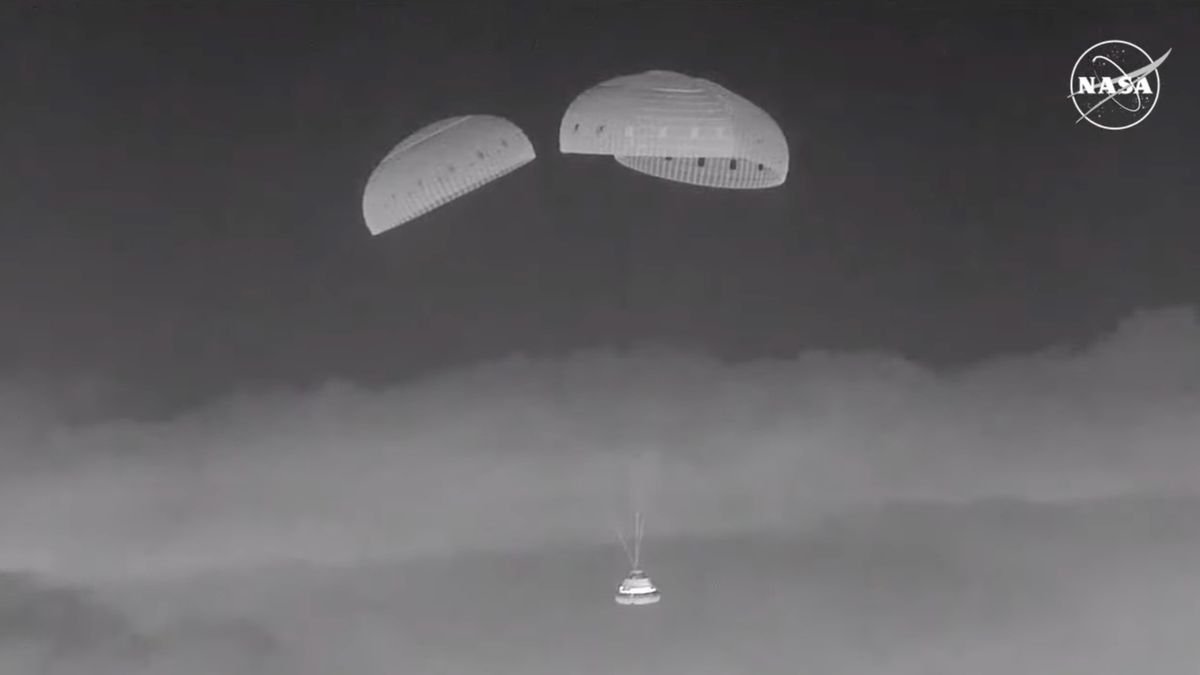 black and white photo of a space capsule descending through a night sky under three parachutes