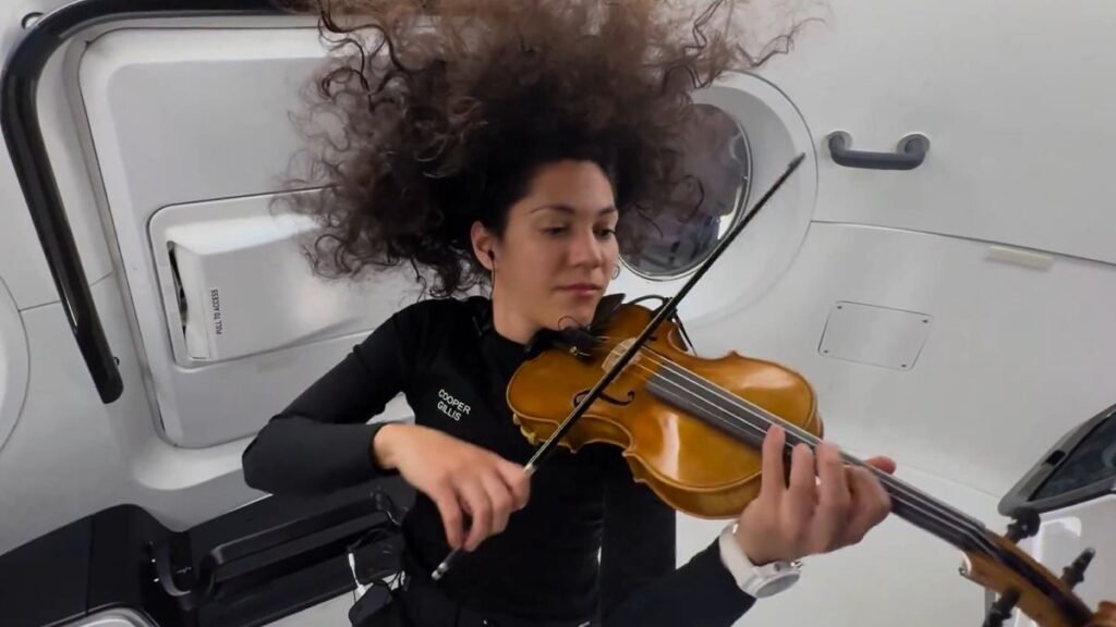 a woman plays violin while floating in zero gravity inside a white spacecraft cabin