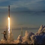 A white and black SpaceX rocket launches into the twilight sky.