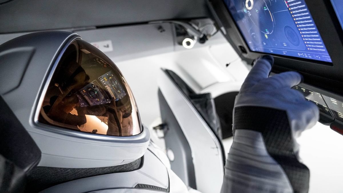 a person in a white spacesuit with a gold facemask touches a touchscreen inside a white spacecraft cockpit