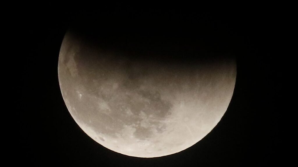 the moon in a dark sky. the top edge of the moon darkened by a shadow