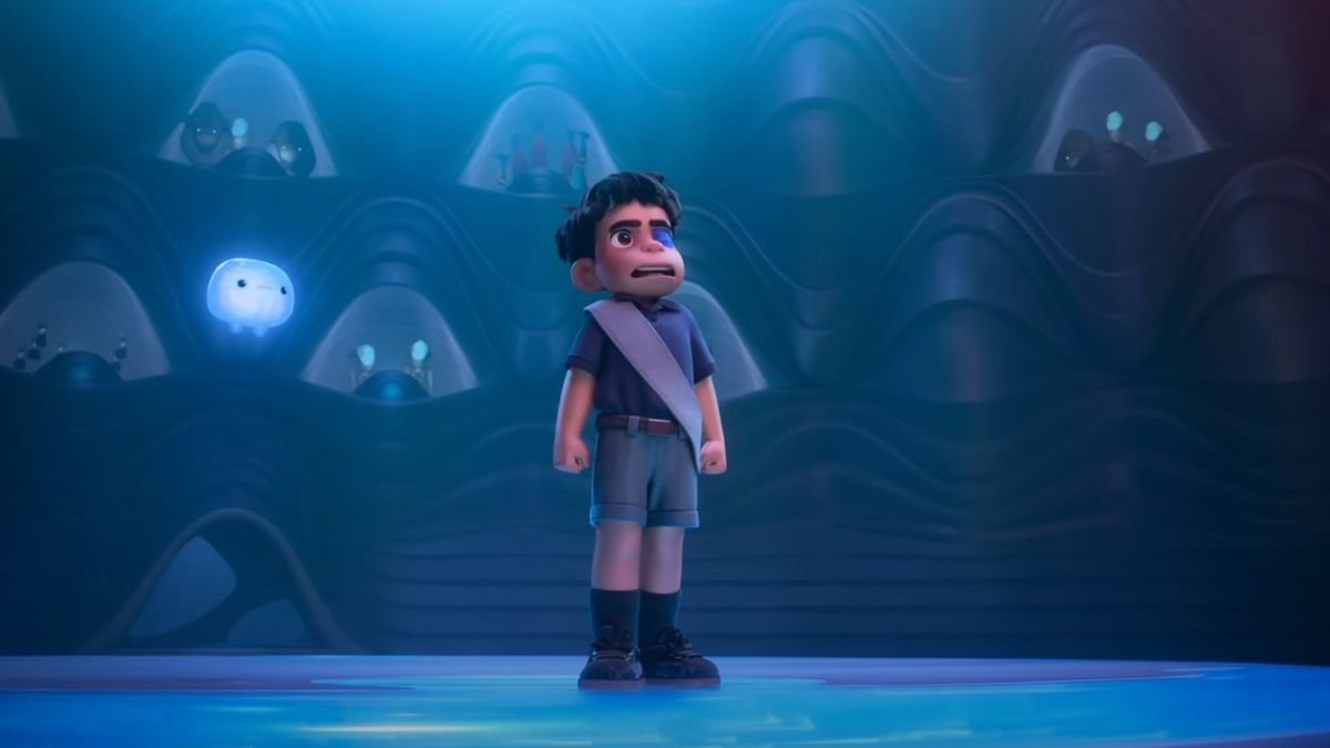 Screenshot from the animated sci-fi movie Elio. A young boy with a blue eye patch stands tall in the center of a giant auditorium as many different aliens stare down at him.