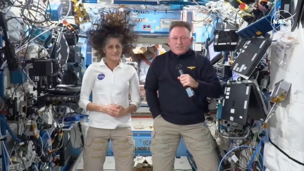 Two people floating in microgravity on the International Space Station. They are surrounded by lots of wires and other hardware.