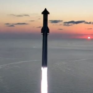 a large rocket launches into a dawn sky from a seaside pad