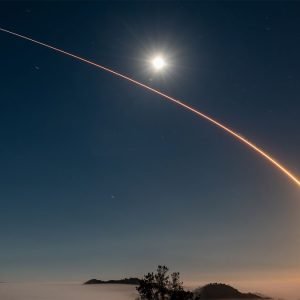 A rocket launch carves an orange arc into a dark night sky in this long-exposure photo.