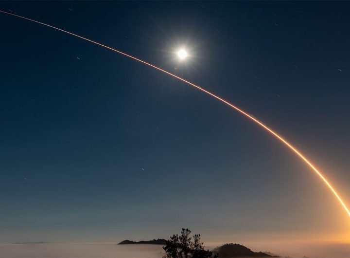 A rocket launch carves an orange arc into a dark night sky in this long-exposure photo.