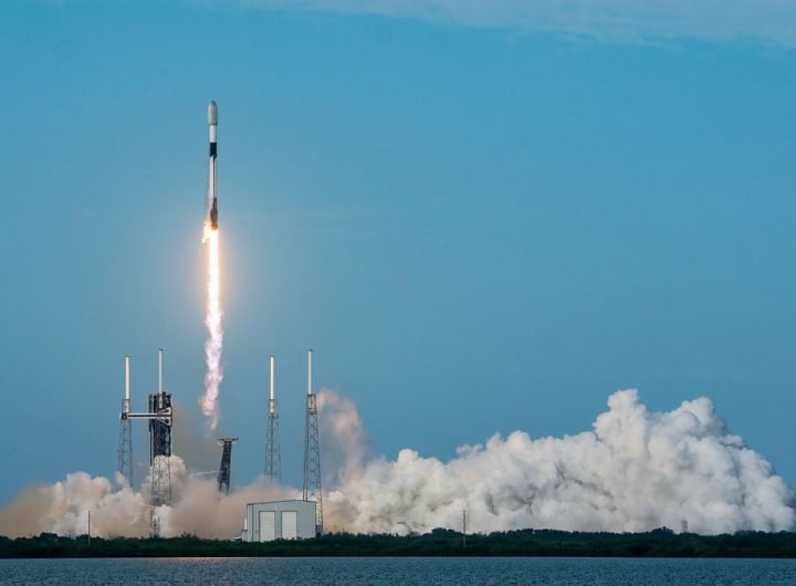 a black-and-white spacex falcon 9 rocket launches into a blue sky.