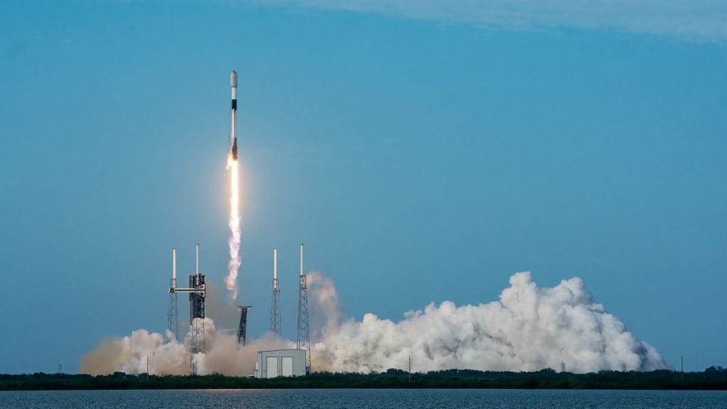 a black-and-white spacex falcon 9 rocket launches into a blue sky.