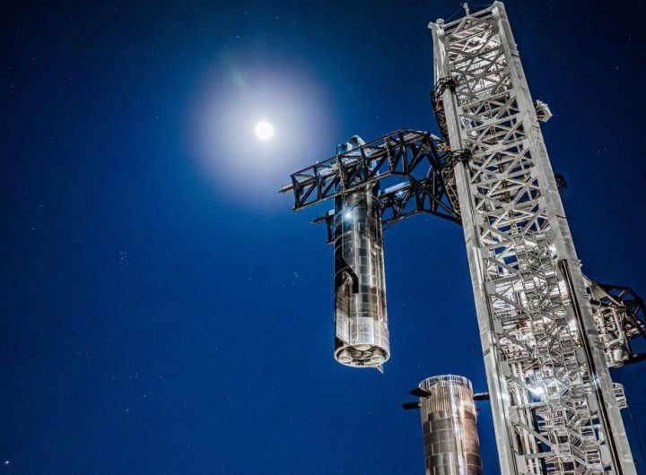 a large silver spacecraft is placed atop a booster by a launch tower at night