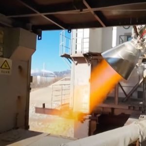 closeup image of a rocket engine firing, producing a streak of orange flame during a ground-based test