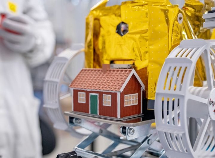 a small model of a red and white house is mounted to a gold foil-covered lunar rover with white wheels